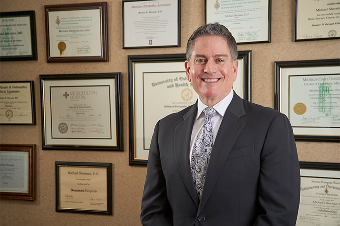 Dr. Sherman in a suit in front of wall of certificates