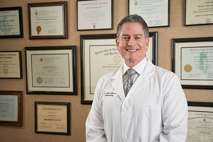 Dr. Sherman in a white coat in front of wall of certificates